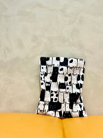 The image shows a cotton tote bag on a bench. The tote bag has cute black and white illustration of rows of cats. However, there are two black and white bunnies hiding among the black and white cat.