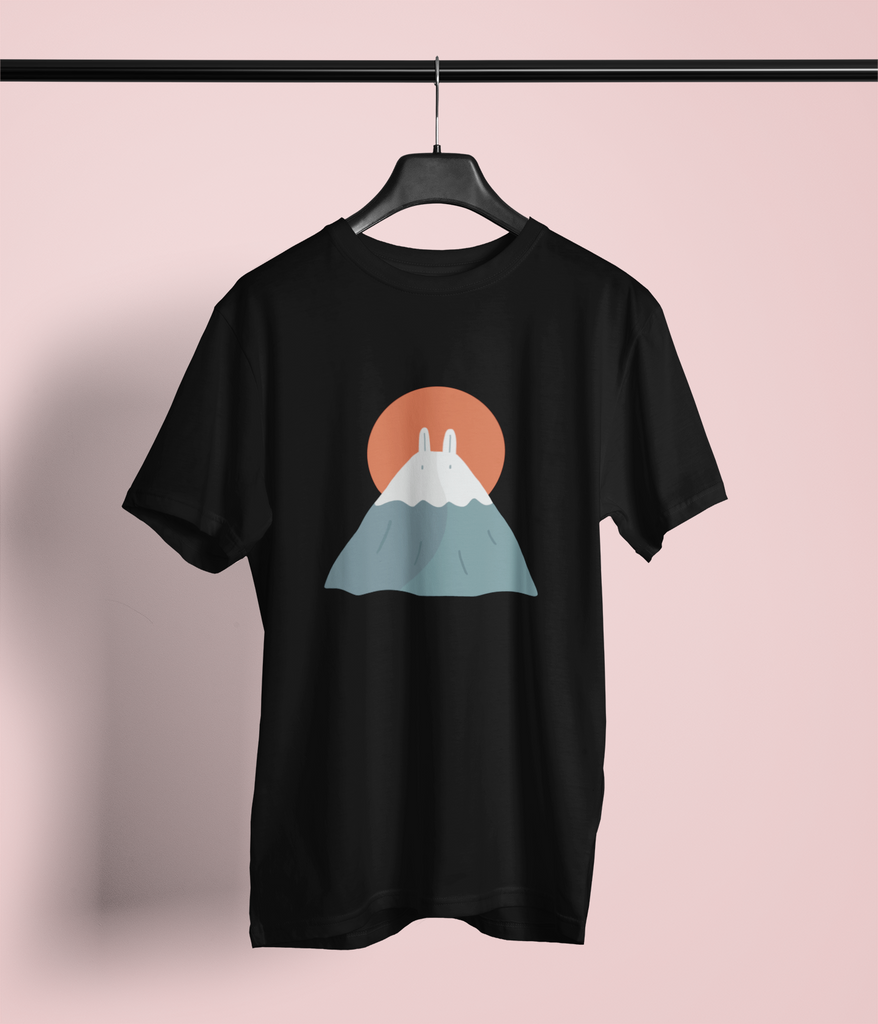 Black T-shirt featuring a minimalist design of Mount Fuji with a pair of bunny ears and a rising orange sun in the background. The t-shirt hangs on a black hanger against a pinkish backdrop