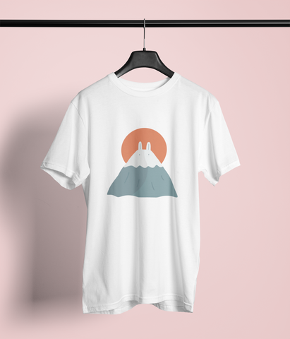 White T-shirt featuring a minimalist design of Mount Fuji with a pair of bunny ears and a rising orange sun in the background. The t-shirt hangs on a black hanger against a pinkish backdrop