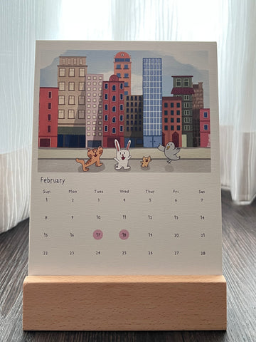 Calendar with The Cat, Bunny, Hamster and Pigeon exploring on a city street, placed on a wooden stand. Singapore public holidays are marked in pink