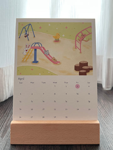 Calendar with a children's illustration of a playground scene on a wooden stand.