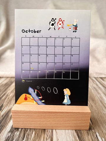 October 2025 calendar inserted in the wooden stand on a desk. The illustration of the October calendar is the story of Alice in Wonderland. There are Alice watching the caterpillar, and white rabbit and card soldiers.