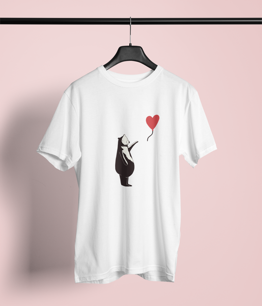 A white T-shirt is displayed on a hanger. The design features a stylized black bear standing on its hind legs, holding a red heart-shaped balloon by its string. This artwork is inspired by Banksy's iconic "Girl with Balloon," giving it a whimsical and playful twist.