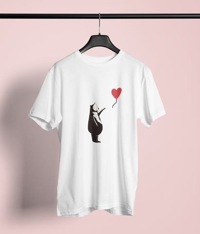 A white T-shirt is displayed on a hanger. The design features a stylized black bear standing on its hind legs, holding a red heart-shaped balloon by its string. This artwork is inspired by Banksy's iconic 