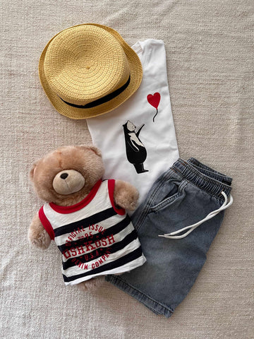 The image shows a children's outfit laid out on a flat surface. It includes a straw hat, a white T-shirt with a design of a black bear holding a red heart-shaped balloon (inspired by Banksy's 