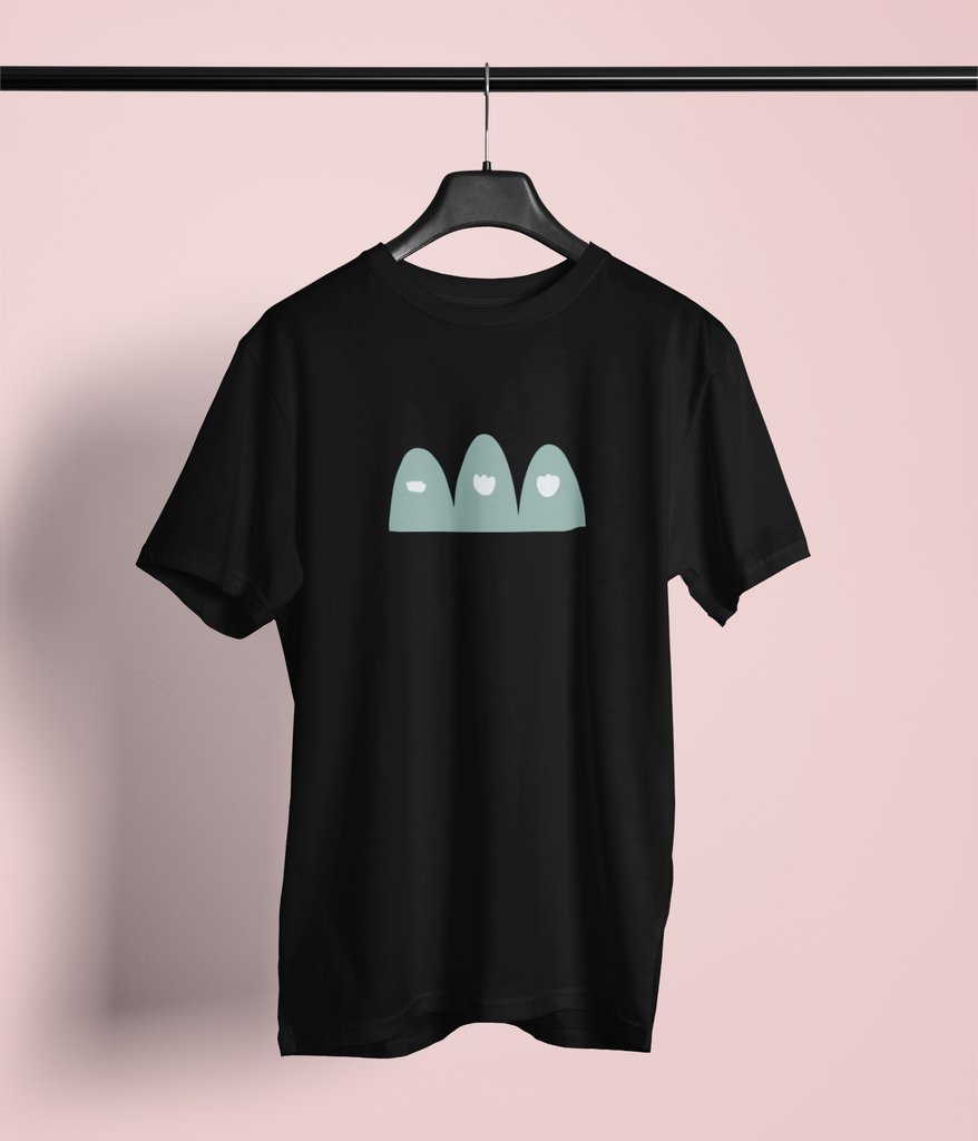 Black T-shirt with a graphic design on the front. The design features three stylized, teal-colored mountains drawn by a child, each with a white cloud near the top, giving them a minimalist and abstract appearance. The T-shirt is displayed on a hanger against a plain background