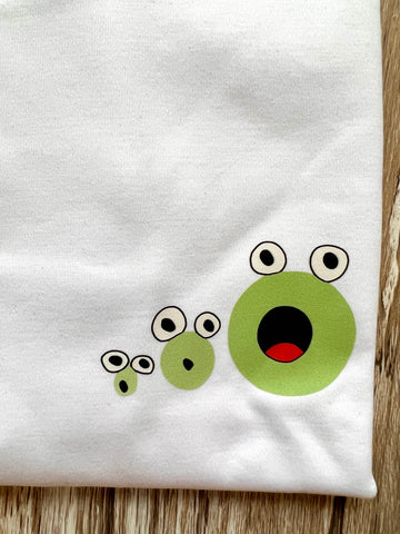 Close up of the t-shirt, showing the illustration of the three frogs. The three frogs from small to big, with their mouths wide open